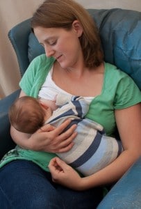 Mother in chair holding nursing baby close to her body