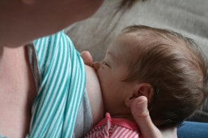 Baby latched on to breast, mother's hand supporting baby's neck