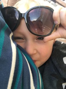 Toddler wearing sunglasses, grinning while breastfeeding