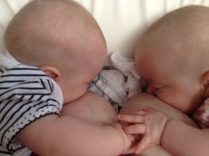 View from above of tandem nursing twin babies holding hands