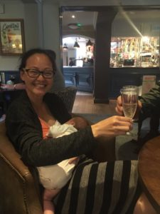 Mother in a bar sitting breastfeeding while raising a glass of wine.