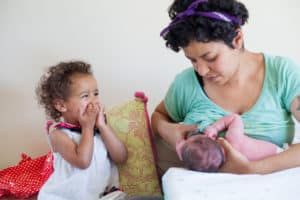 Mother nursing her newborn with excited toddler looking on with a look of joy