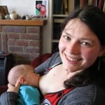 Baby feeding with an at-breast supplementer, mum is smiling