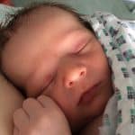 Newborn asleep on mothers chest with hospital gown over the top